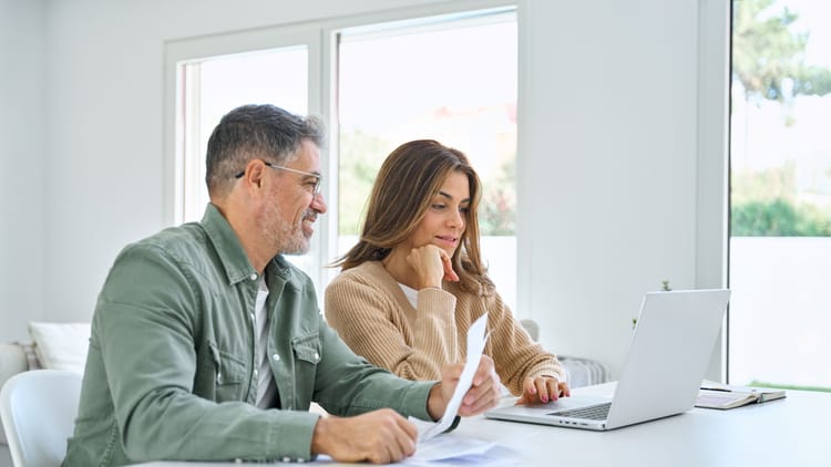 happy middle aged couple deciding on RV rental vs buying by sitting in front of laptop and going though finances